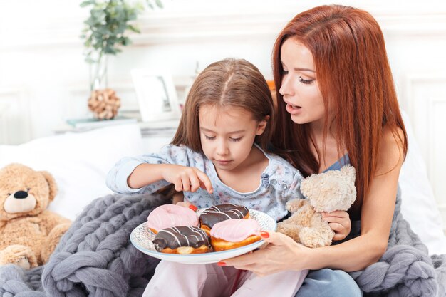 bambina carina godendo, giocando e creando con la torta con la madre