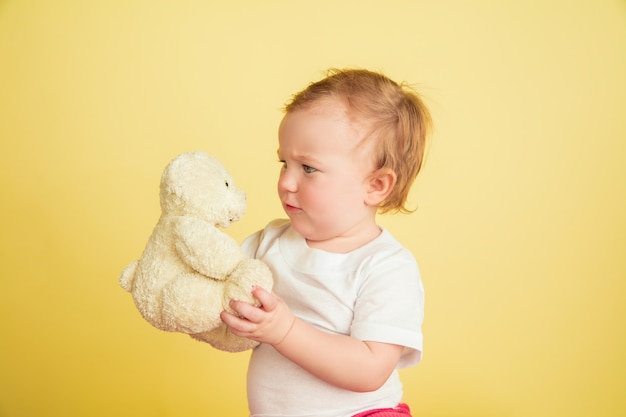 Bambina caucasica, bambini isolati su sfondo giallo studio. Ritratto di bambino carino e adorabile, bambino che gioca con l'orsacchiotto. Concetto di infanzia, famiglia, felicità, nuova vita, educazione.