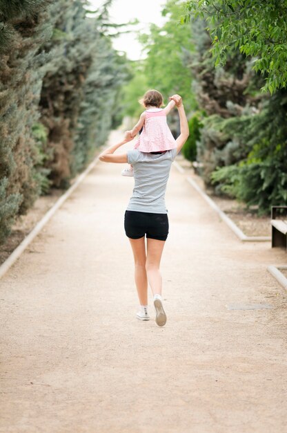 Bambina che cammina sulle spalle di sua madre nel parco