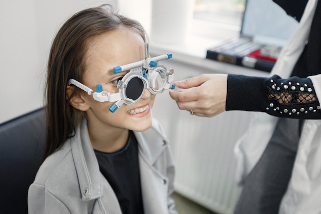 Bambina che controlla la sua vista al centro di oftalmologia. Ottico optometrista femminile che esegue test della vista. Ragazza bruna che indossa giacca grigia e camicia nera.