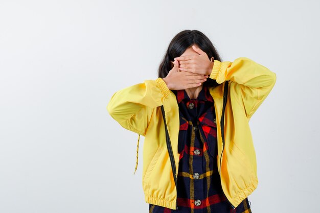 Bambina che copre il viso con le mani in camicia a quadri, giacca e sguardo malinconico