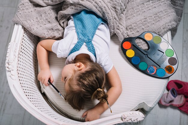 Bambina che dorme sul divano con la tavolozza di aquarelle