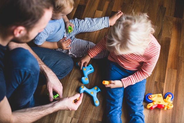 Bambina che esamina i pezzi di un giocattolo con il padre e il fratello