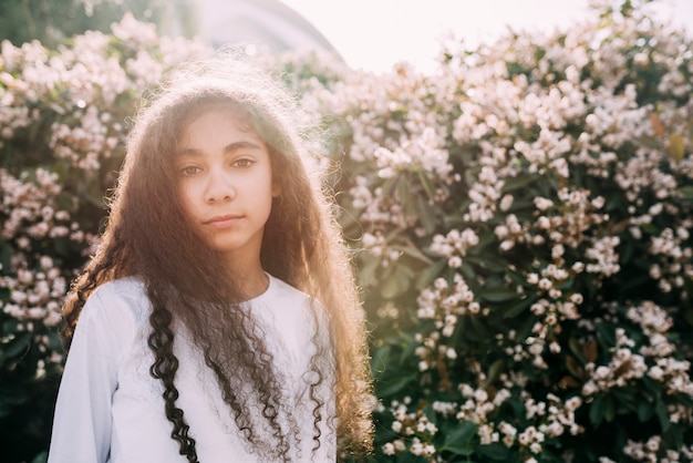 Bambina che esamina macchina fotografica che sta contro il giacimento di fiore