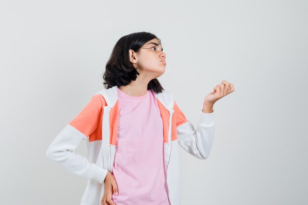 Bambina che fa gesto di soldi in t-shirt, giacca e sembra indigente. vista frontale.