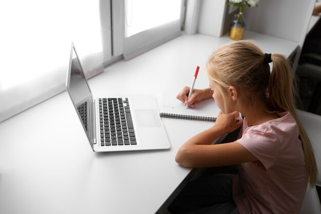 Bambina che fa i compiti a casa con laptop e notebook