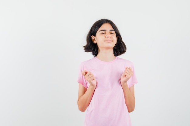 Bambina che fa meditazione con gli occhi chiusi in maglietta rosa e cerca pacifica, vista frontale.