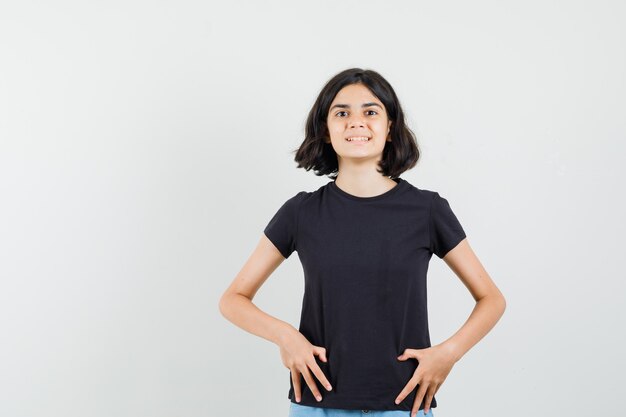 Bambina che guarda davanti in maglietta nera, pantaloncini e sembra allegra. vista frontale.