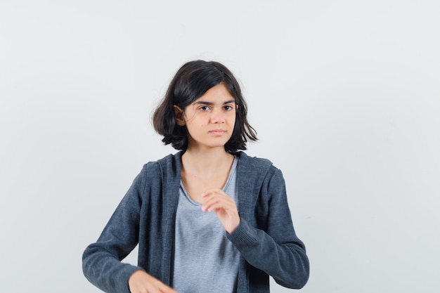 Bambina che guarda lontano in t-shirt, giacca e sembra sognante, vista frontale.