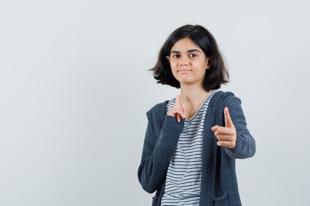 Bambina che indica alla macchina fotografica in t-shirt, giacca e guardando fiducioso,