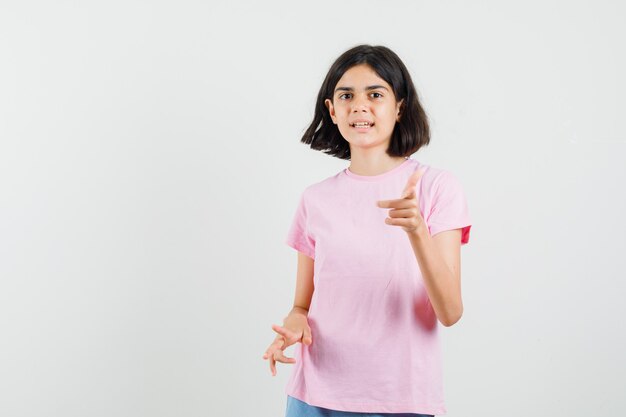 Bambina che indica davanti in maglietta rosa, pantaloncini, vista frontale.