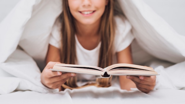 Bambina che legge un libro a letto
