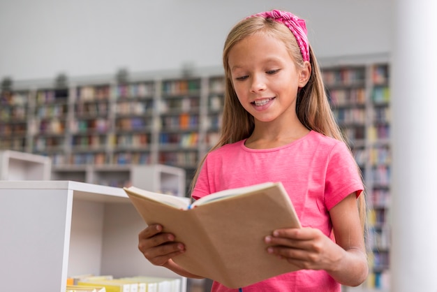 Bambina che legge un libro in biblioteca