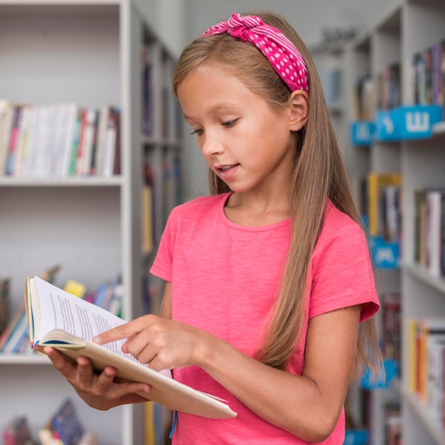 Bambina che legge un libro in biblioteca