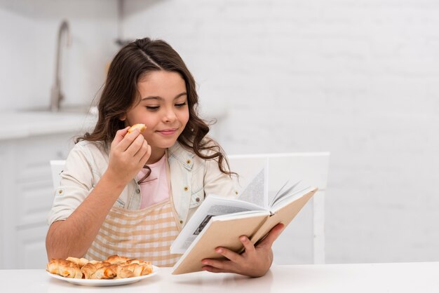 Bambina che legge un libro in cucina