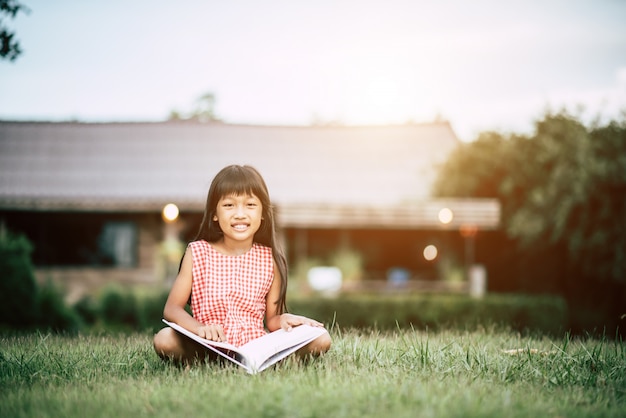 Bambina che legge un libro nel giardino di casa