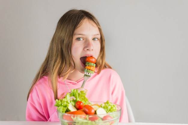 Bambina che mangia prima colazione sana contro fondo bianco