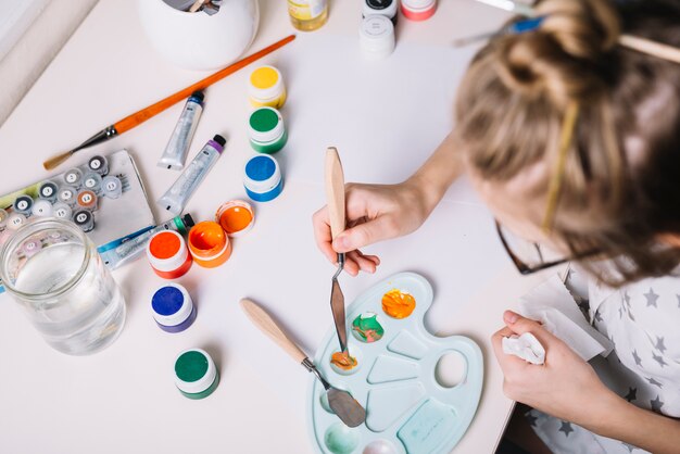 Bambina che mescola gouache sulla tavolozza al tavolo