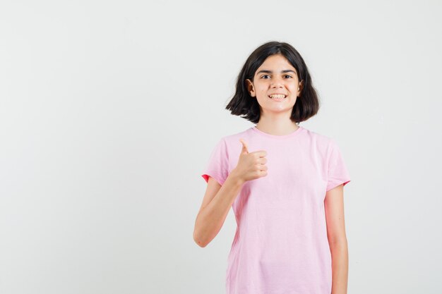 Bambina che mostra il pollice in su in maglietta rosa e che sembra felice. vista frontale.