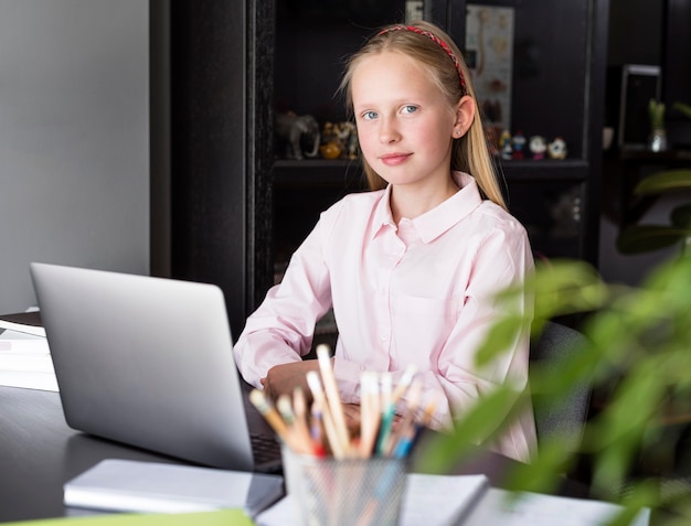 Bambina che posa accanto al suo computer portatile