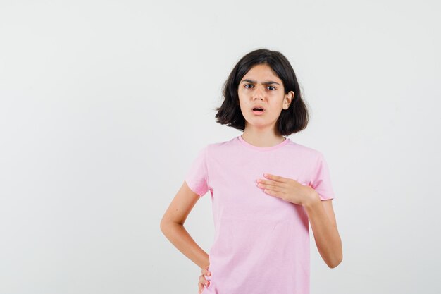 Bambina che punta a se stessa in maglietta rosa e che sembra perplessa. vista frontale.