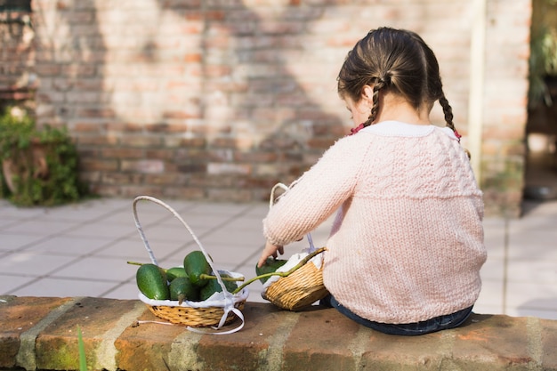 Bambina che si siede sulla parete che raccoglie merce nel carrello dell&#39;avocado