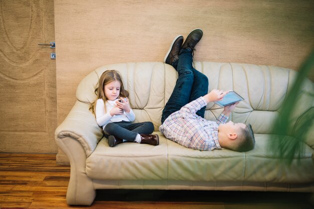 Bambina che si siede vicino a suo fratello guardando la tavoletta digitale sul divano a casa