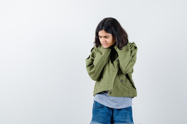 Bambina che si tiene per mano sulla testa in cappotto, t-shirt, jeans e sembra esausta. vista frontale.