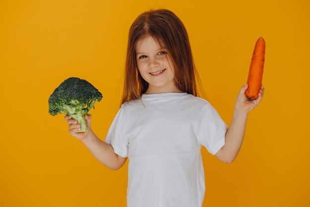 Bambina che tiene broccoli e carote