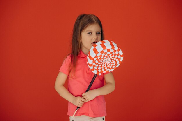 Bambina che tiene grande lecca-lecca isolato su sfondo rosso