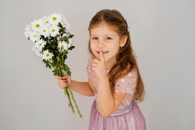 Bambina che tiene il mazzo di fiori primaverili e chiede silenzio
