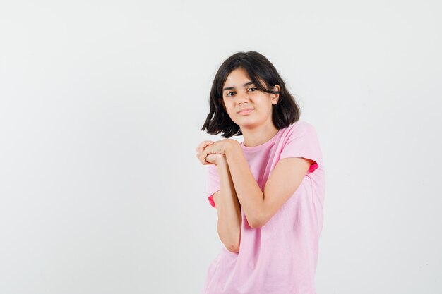 Bambina che tiene le mani giunte in maglietta rosa e che sembra carina, vista frontale.
