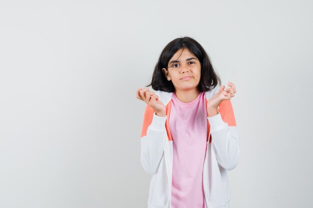 Bambina che tiene le mani in un gesto confuso alzando le spalle in t-shirt, giacca