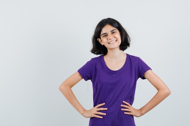 Bambina che tiene le mani sulla vita in maglietta e sembra allegra,