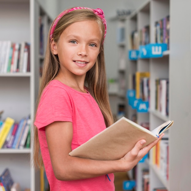 Bambina che tiene un libro in biblioteca