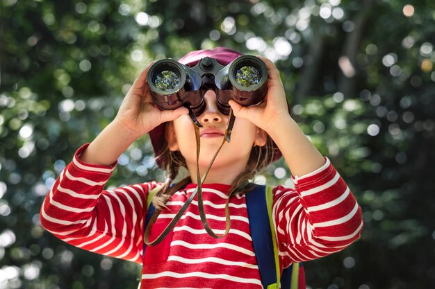 Bambina che usa il binocolo nella foresta