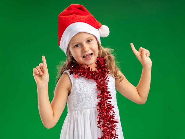 Bambina colpita che indossa il cappello di Natale con la ghirlanda sui punti del collo in alto isolato su sfondo verde