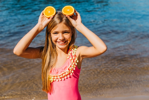 Bambina con fette d&#39;arancia facendo orecchie sulla spiaggia