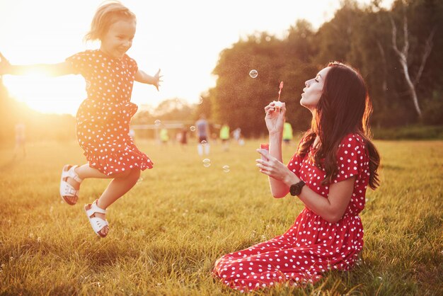 Bambina con le bolle con sua madre nel parco al tramonto.