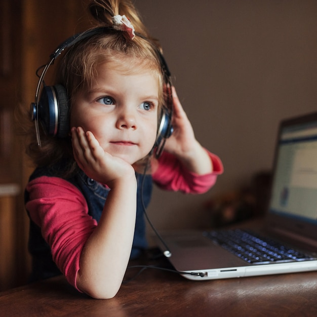 bambina con le cuffie che ascolta la musica, utilizzando il computer portatile