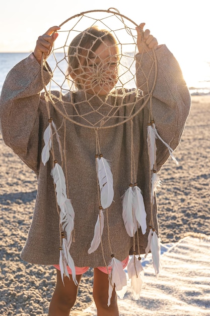 Bambina con un acchiappasogni in riva al mare al tramonto