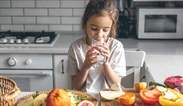Bambina con un bicchiere d'acqua in una cucina con frutta e verdura