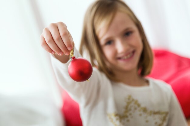 Bambina con una palla di Natale rossa in mano