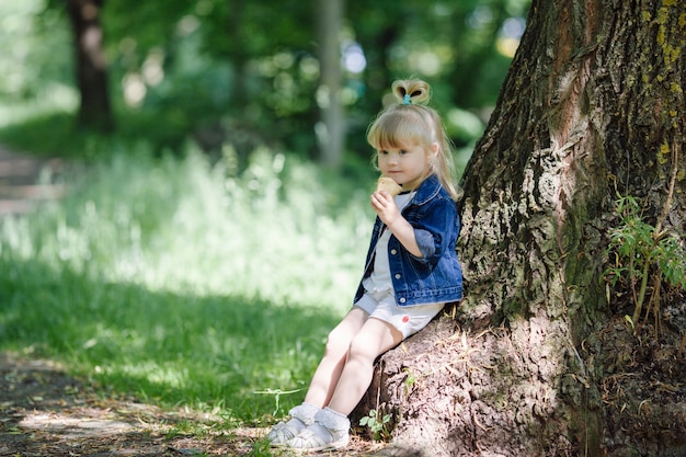 Bambina di mangiare un gelato appoggiato a un albero