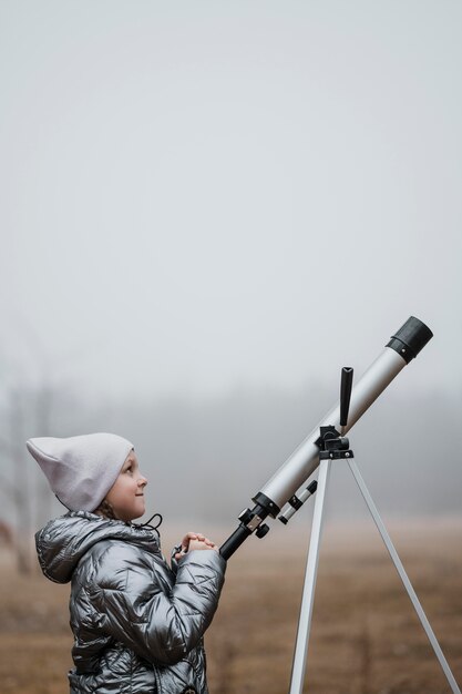 Bambina di vista laterale usando un telescopio