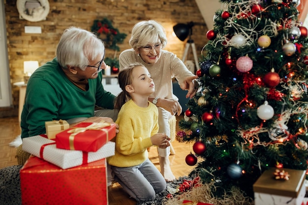 Bambina e nonni che decorano insieme l'albero di Natale a casa