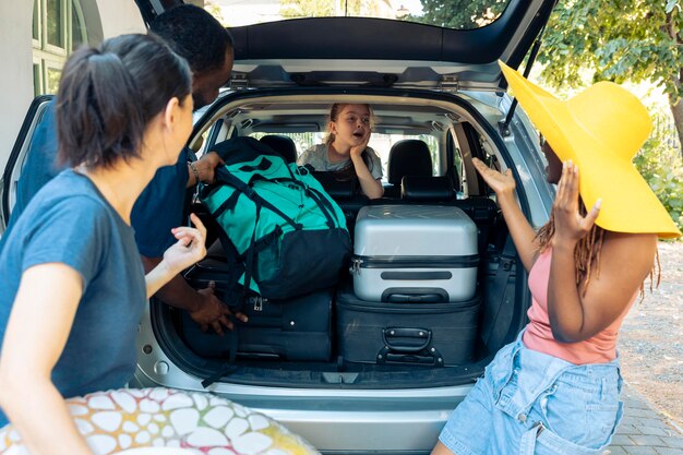 Bambina e persone diverse che vanno in vacanza, caricando borse da viaggio nel bagagliaio del veicolo. Partire per l'avventura in vacanza con la famiglia e gli amici, mettere la valigia o il carrello in automobile prima del viaggio.