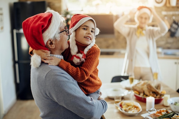 Bambina felice che abbraccia il nonno mentre trascorre il giorno di Natale insieme a casa