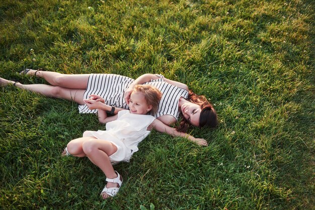 Bambina felice e sua madre divertendosi all'aperto sull'erba verde nel giorno di estate soleggiato.