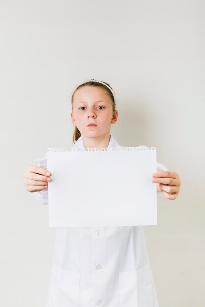 Bambina ferma che tiene foglio di carta bianca